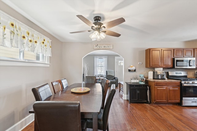 dining space featuring arched walkways, ceiling fan, baseboards, and dark wood finished floors