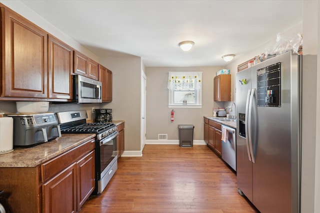 kitchen with a sink, wood finished floors, appliances with stainless steel finishes, baseboards, and visible vents