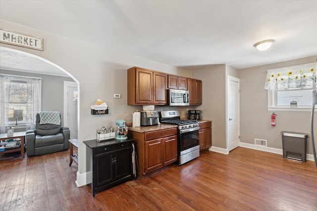 kitchen featuring arched walkways, dark wood-style floors, visible vents, appliances with stainless steel finishes, and brown cabinets