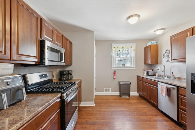 kitchen featuring a sink, wood finished floors, appliances with stainless steel finishes, baseboards, and visible vents
