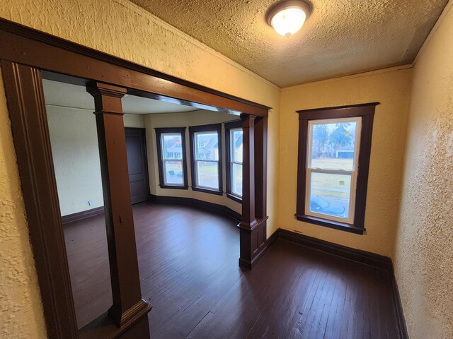 3491 Garland St, Detroit, MI 48214 - unfurnished room featuring baseboards, dark wood finished floors, a textured wall, a textured ceiling, and ornate columns