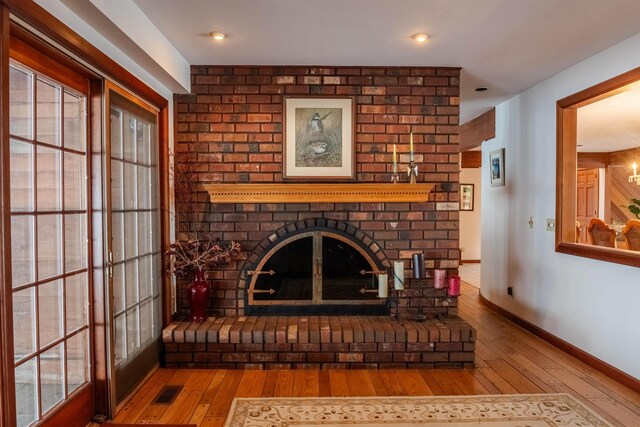 living area with a brick fireplace, baseboards, and hardwood / wood-style floors