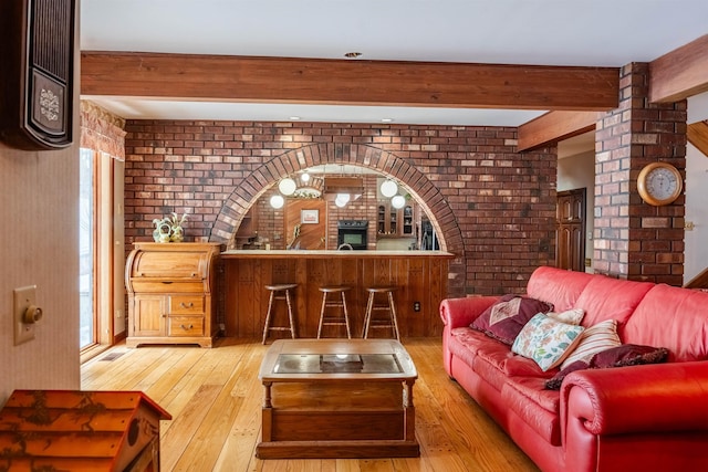 living area featuring beamed ceiling, hardwood / wood-style floors, and brick wall