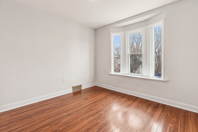 unfurnished room featuring wood finished floors, baseboards, and visible vents