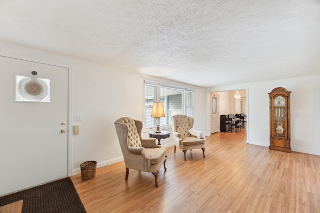 sitting room featuring baseboards, light wood-style flooring, and a textured ceiling