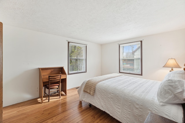 bedroom featuring a textured ceiling, multiple windows, and wood finished floors