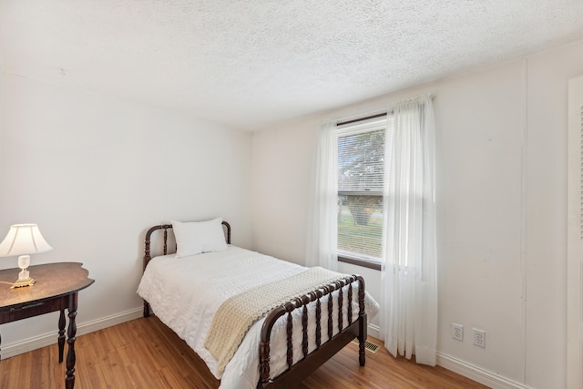 bedroom featuring a textured ceiling, baseboards, and light wood-style flooring