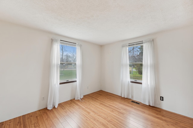 spare room with visible vents, a textured ceiling, light wood-style flooring, and a healthy amount of sunlight
