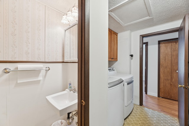 washroom featuring a textured ceiling, independent washer and dryer, cabinet space, a sink, and light wood-style flooring