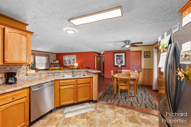 kitchen with ceiling fan, a wainscoted wall, a peninsula, stainless steel appliances, and a sink
