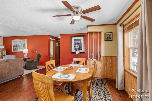 dining area with hardwood / wood-style flooring, wallpapered walls, a textured ceiling, crown molding, and wainscoting