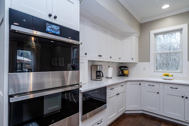kitchen with crown molding, light countertops, decorative backsplash, stainless steel double oven, and white cabinetry