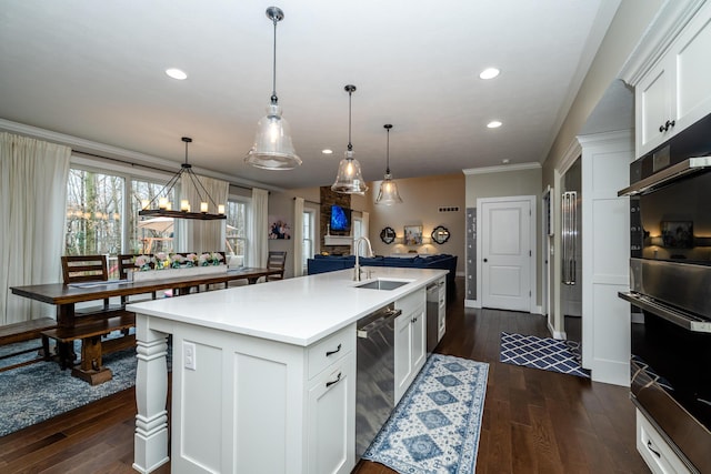 kitchen featuring an island with sink, ornamental molding, a sink, dark wood finished floors, and stainless steel appliances