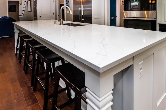 kitchen featuring light stone countertops, dark wood finished floors, double oven, a kitchen bar, and a sink