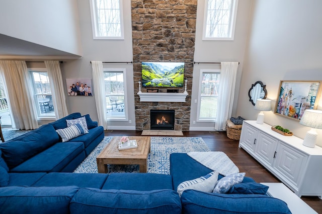 living room featuring a fireplace, dark wood-type flooring, a healthy amount of sunlight, and a towering ceiling