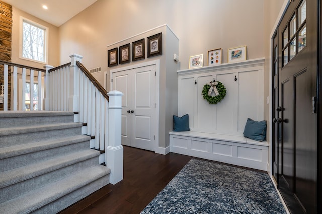 mudroom with a high ceiling, a decorative wall, dark wood-style floors, and visible vents