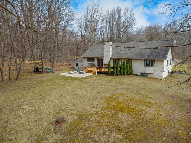 rear view of house with roof with shingles, a wooden deck, a chimney, and a lawn