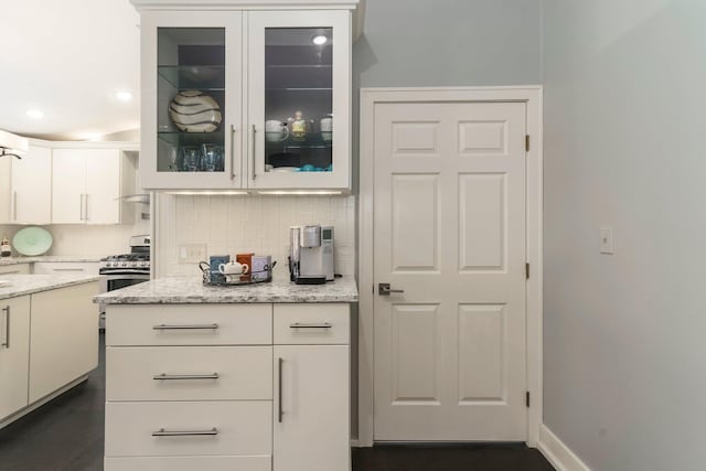 kitchen featuring white cabinetry, glass insert cabinets, stainless steel range with gas cooktop, and backsplash