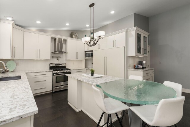kitchen featuring a sink, built in appliances, wall chimney range hood, white cabinetry, and decorative backsplash