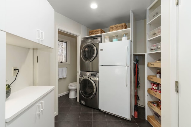 washroom featuring baseboards, laundry area, stacked washer and clothes dryer, and dark tile patterned floors