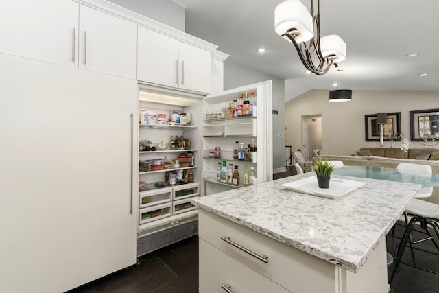 kitchen featuring lofted ceiling, light stone counters, pendant lighting, white cabinetry, and a kitchen island