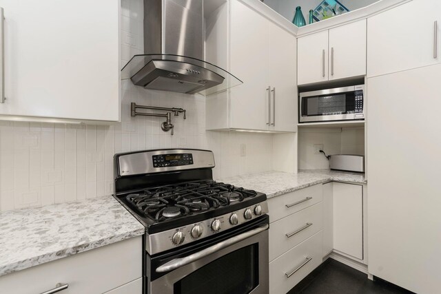 kitchen with light stone counters, wall chimney exhaust hood, decorative backsplash, white cabinets, and appliances with stainless steel finishes