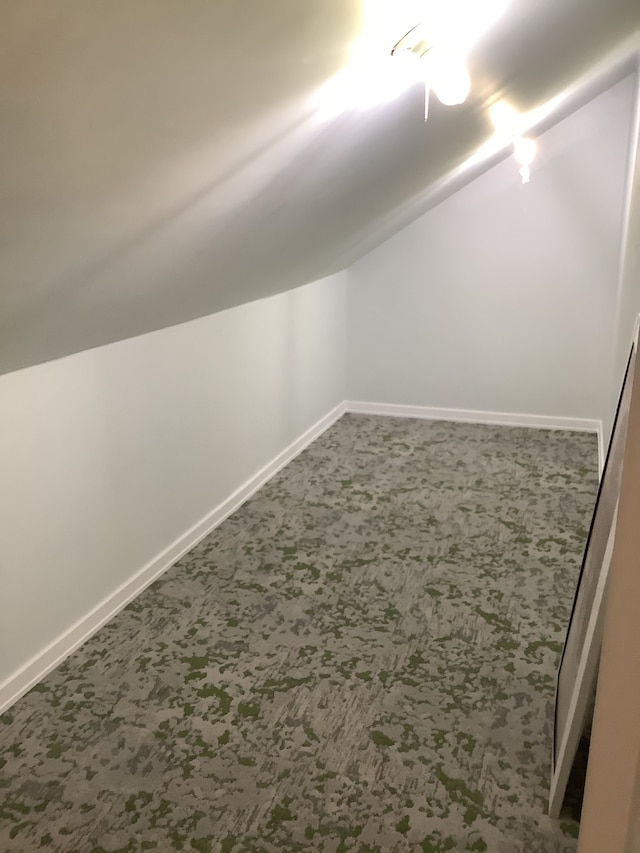 additional living space with dark carpet, baseboards, and lofted ceiling
