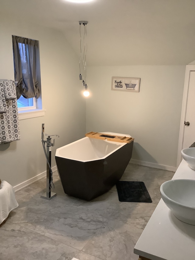 full bathroom with double vanity, a freestanding tub, baseboards, and a sink