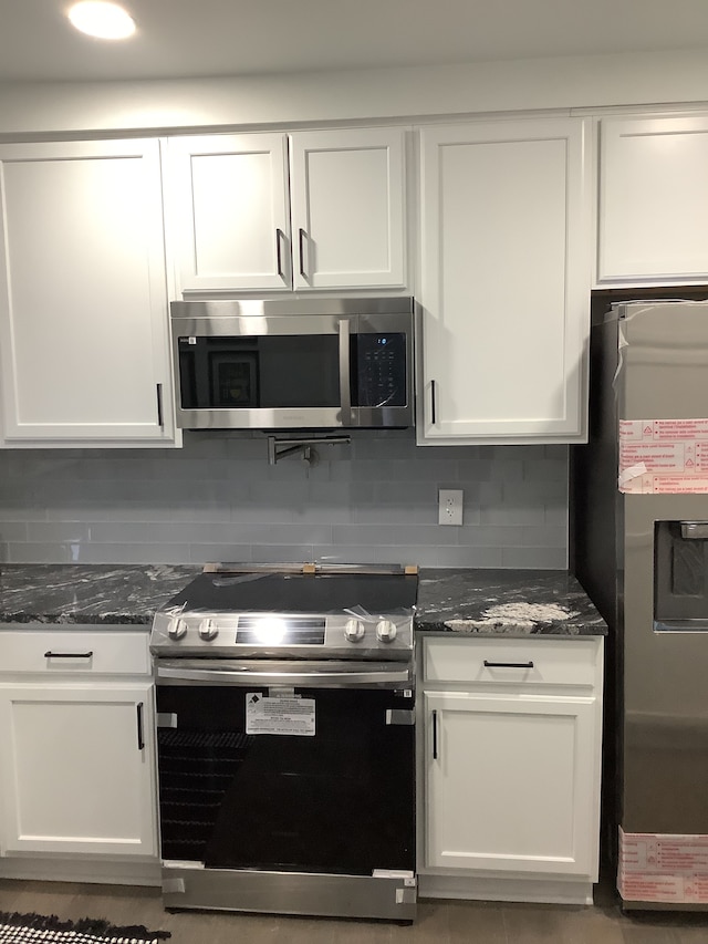 kitchen with decorative backsplash, dark stone countertops, white cabinetry, and stainless steel appliances