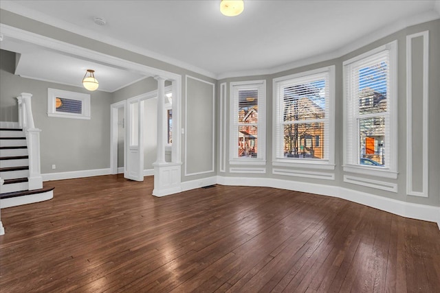 empty room with dark wood-style floors, baseboards, decorative columns, ornamental molding, and stairs