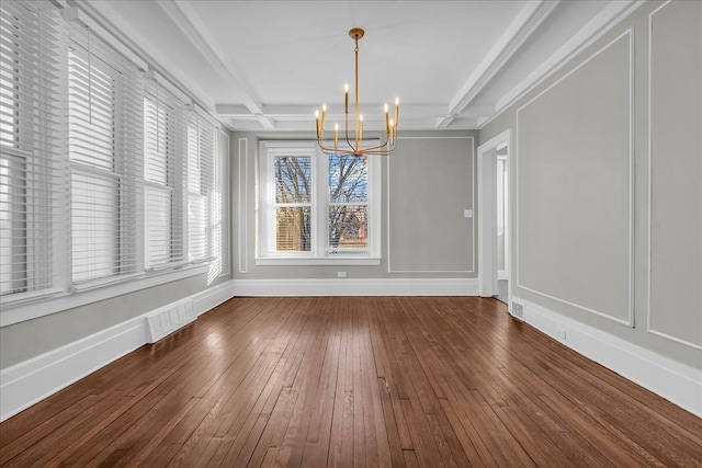 unfurnished dining area featuring beam ceiling, hardwood / wood-style flooring, coffered ceiling, an inviting chandelier, and baseboards