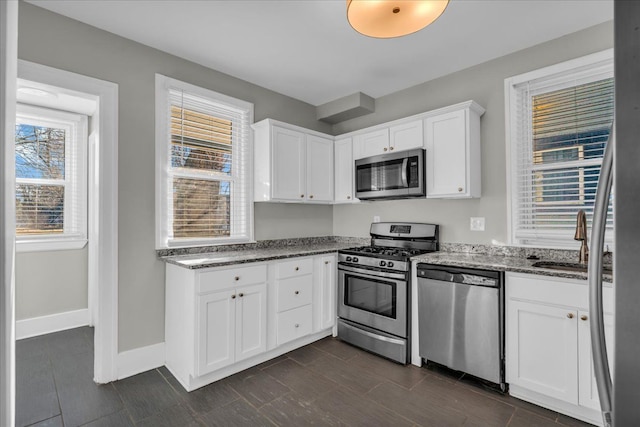 kitchen with dark stone countertops, appliances with stainless steel finishes, white cabinets, and a sink