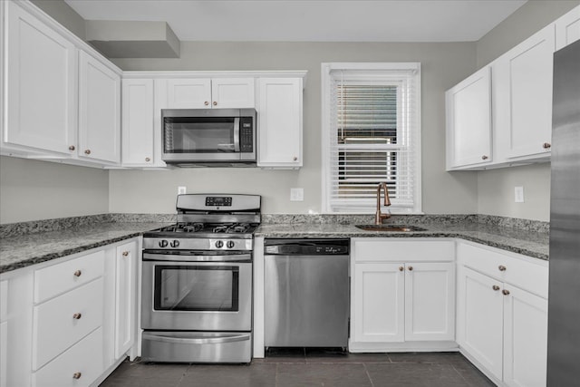 kitchen with white cabinets, stone countertops, appliances with stainless steel finishes, and a sink