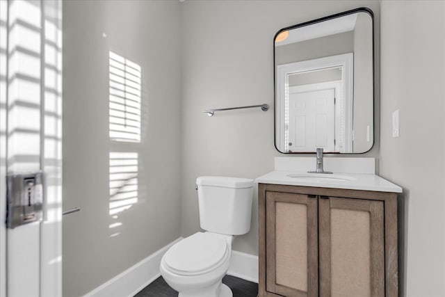 half bathroom with baseboards, toilet, and vanity