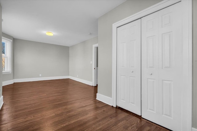 unfurnished bedroom featuring a closet, dark wood-type flooring, and baseboards