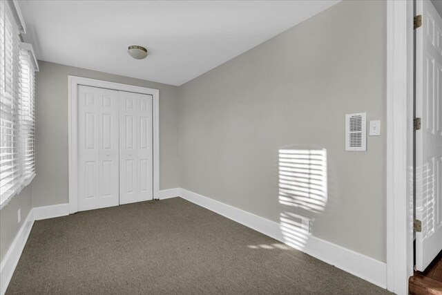 unfurnished bedroom with visible vents, multiple windows, baseboards, and dark colored carpet