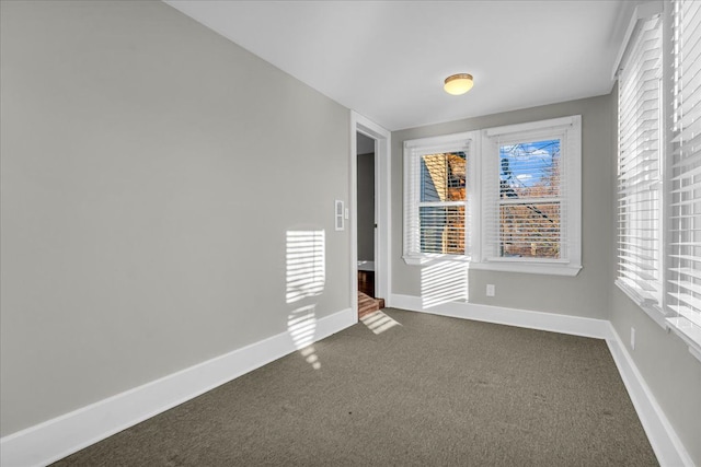 spare room featuring baseboards and dark colored carpet