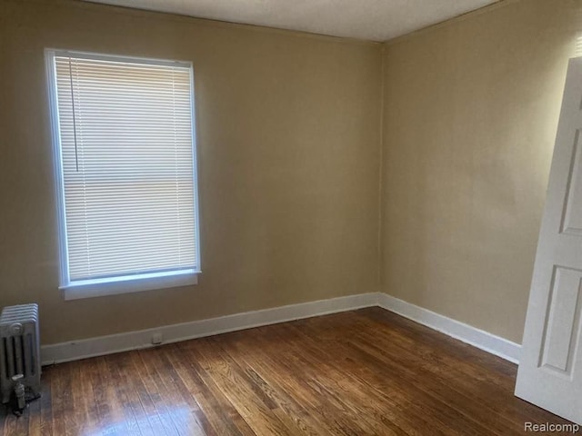 spare room with baseboards, radiator heating unit, and dark wood-type flooring