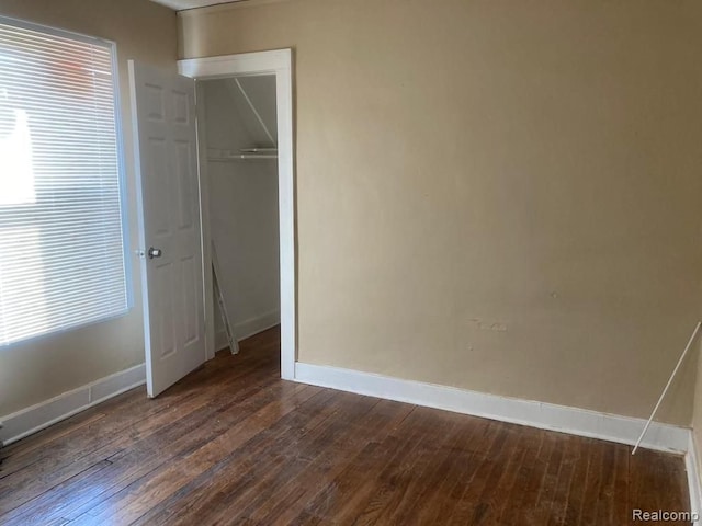 unfurnished bedroom with dark wood-style flooring, baseboards, and a closet