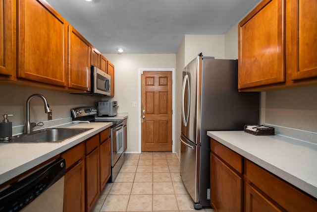 kitchen with brown cabinets, a sink, appliances with stainless steel finishes, light countertops, and light tile patterned floors