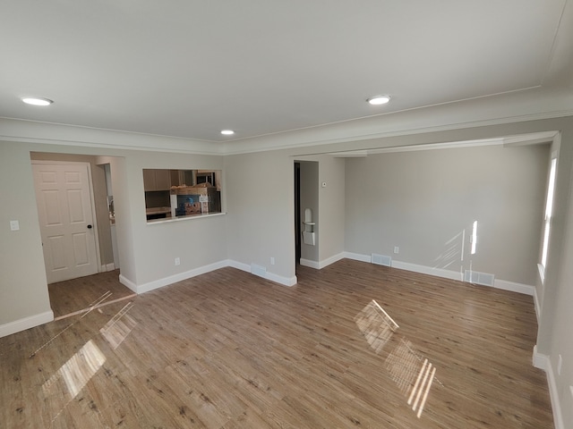 unfurnished living room featuring wood finished floors, baseboards, ornamental molding, and recessed lighting