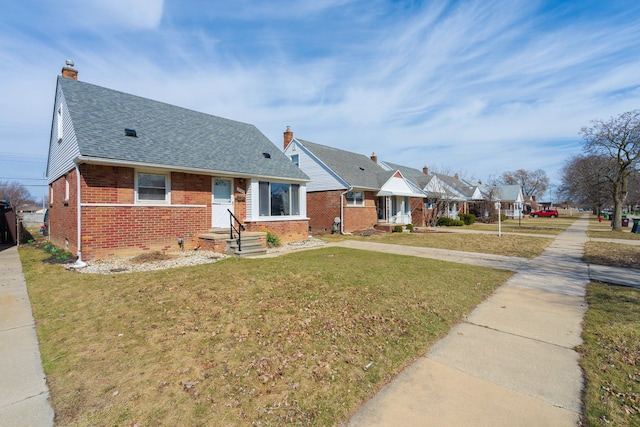 view of front of property featuring brick siding, a shingled roof, a front yard, and a chimney