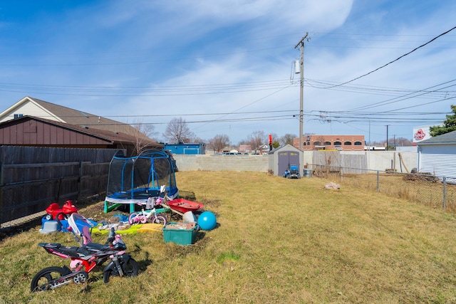 view of yard featuring a fenced backyard, an outbuilding, a storage unit, and a trampoline