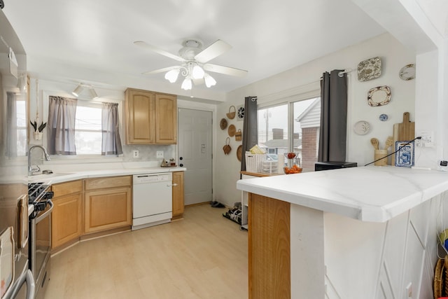 kitchen with white dishwasher, a sink, light wood finished floors, a peninsula, and stainless steel range with gas stovetop