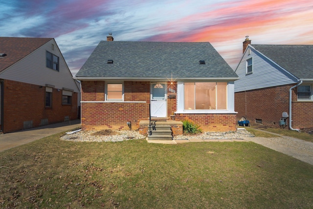 bungalow-style house with a front lawn, brick siding, a shingled roof, and a chimney