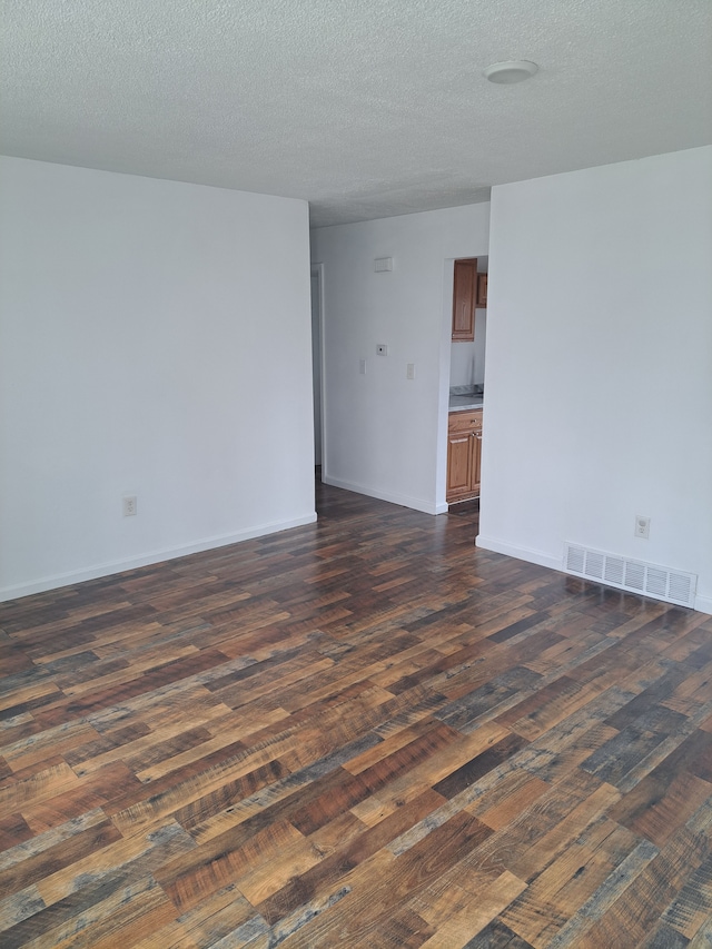 empty room with visible vents, baseboards, a textured ceiling, and dark wood-style floors
