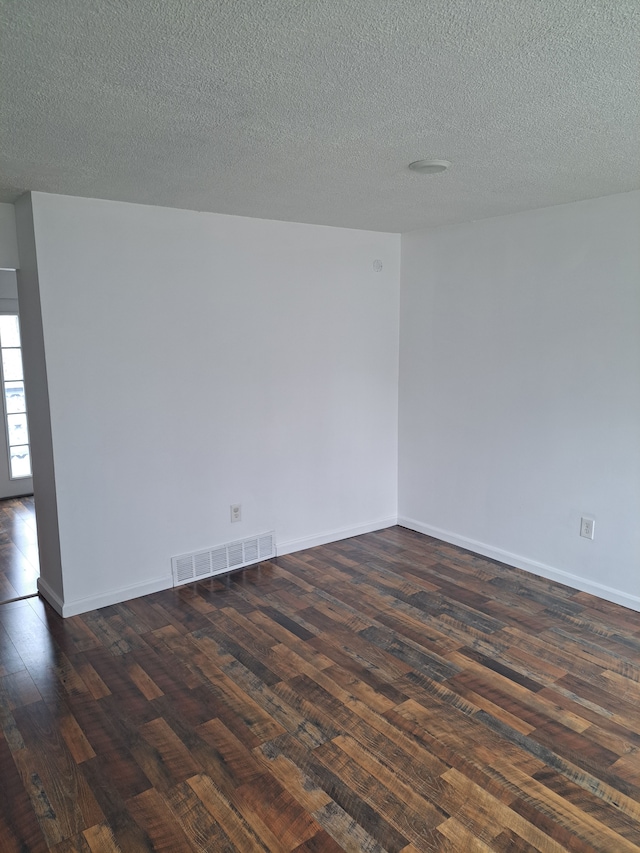 spare room featuring visible vents, a textured ceiling, baseboards, and dark wood-style flooring