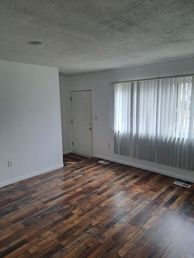 empty room with plenty of natural light, visible vents, dark wood-type flooring, and baseboards