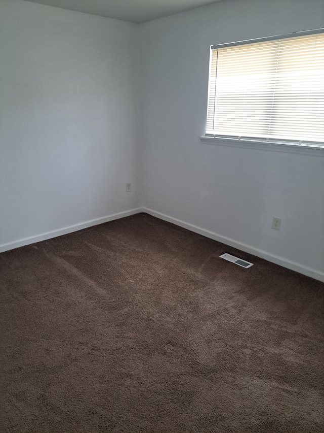 spare room with visible vents, dark carpet, and baseboards