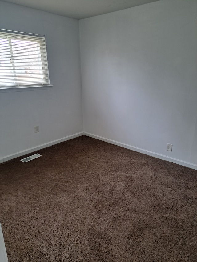 unfurnished room featuring dark colored carpet, visible vents, and baseboards